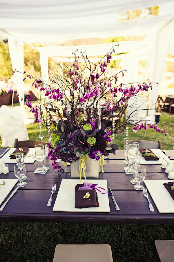 Reception table centerpiece with purple, light green, and yellow flowers with dangling crystal arrangements - photo by Orange County based wedding photographers Mark Brooke